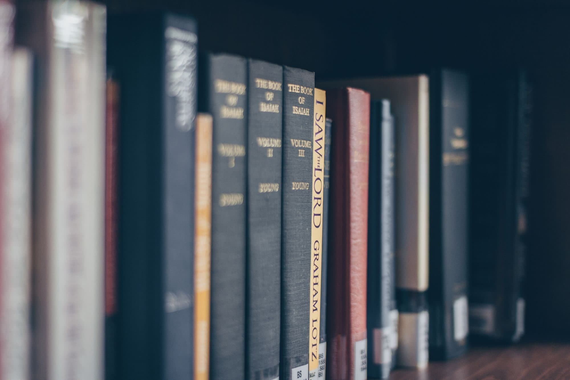 Dorsi di libri allineati su uno scaffale, in penombra